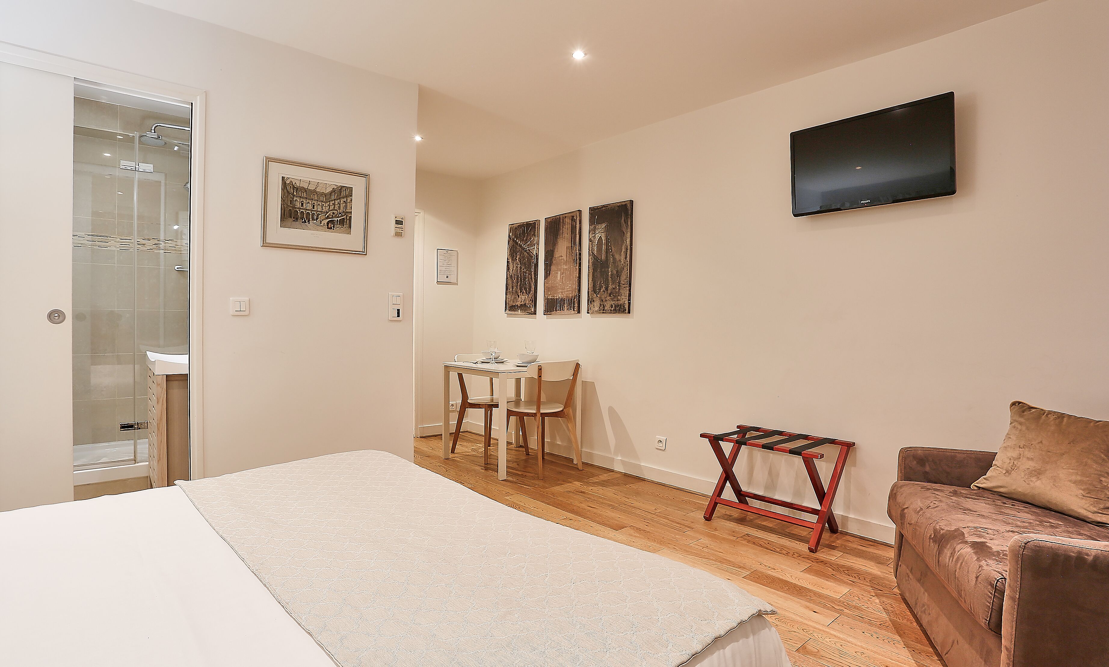 A bedroom with a bed, a desk, a chair, a TV, and artwork on the wall.