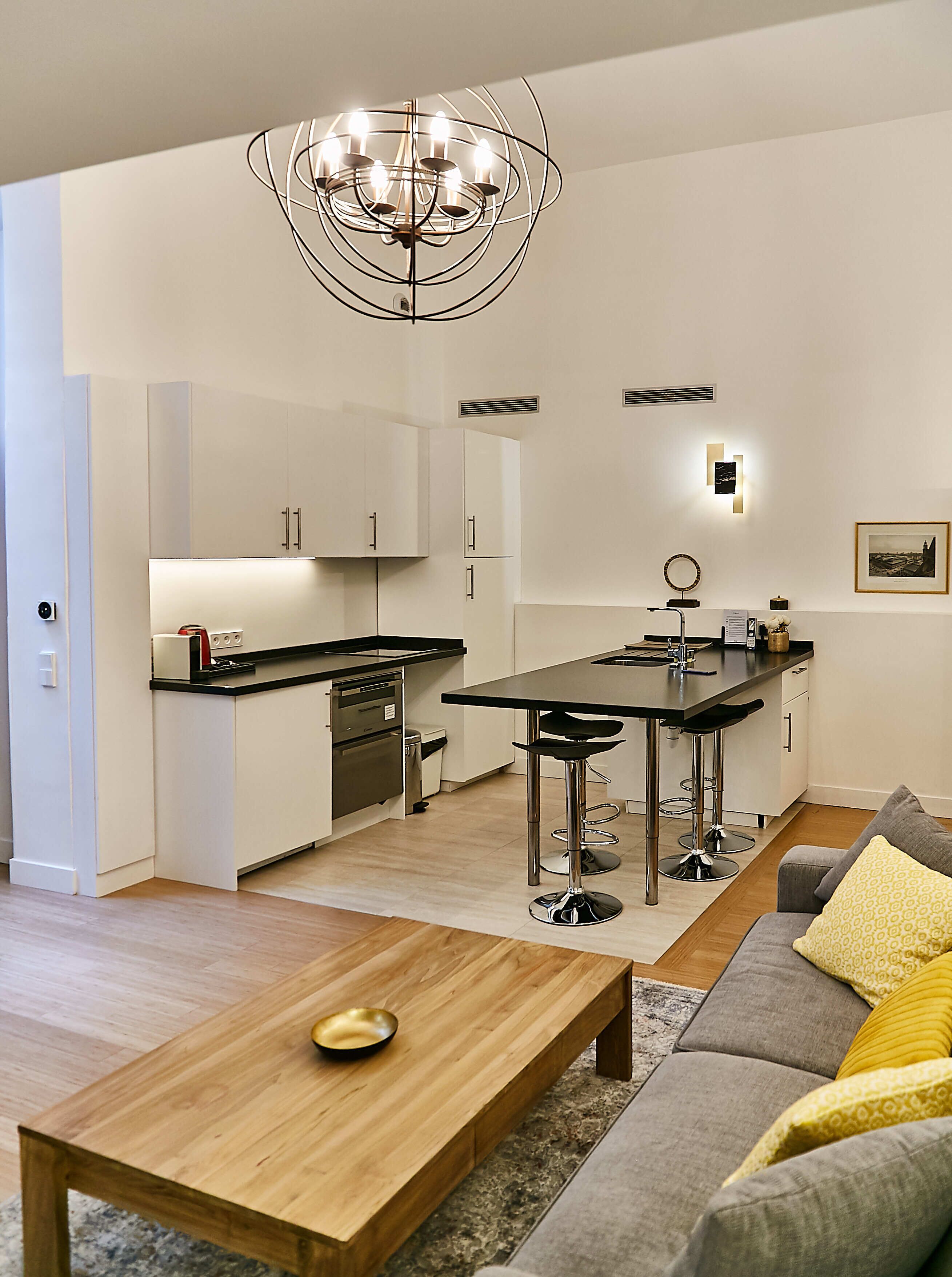 Una cucina moderna con isola centrale, una zona pranzo con tavolo in legno e un soggiorno con divano e tavolino.