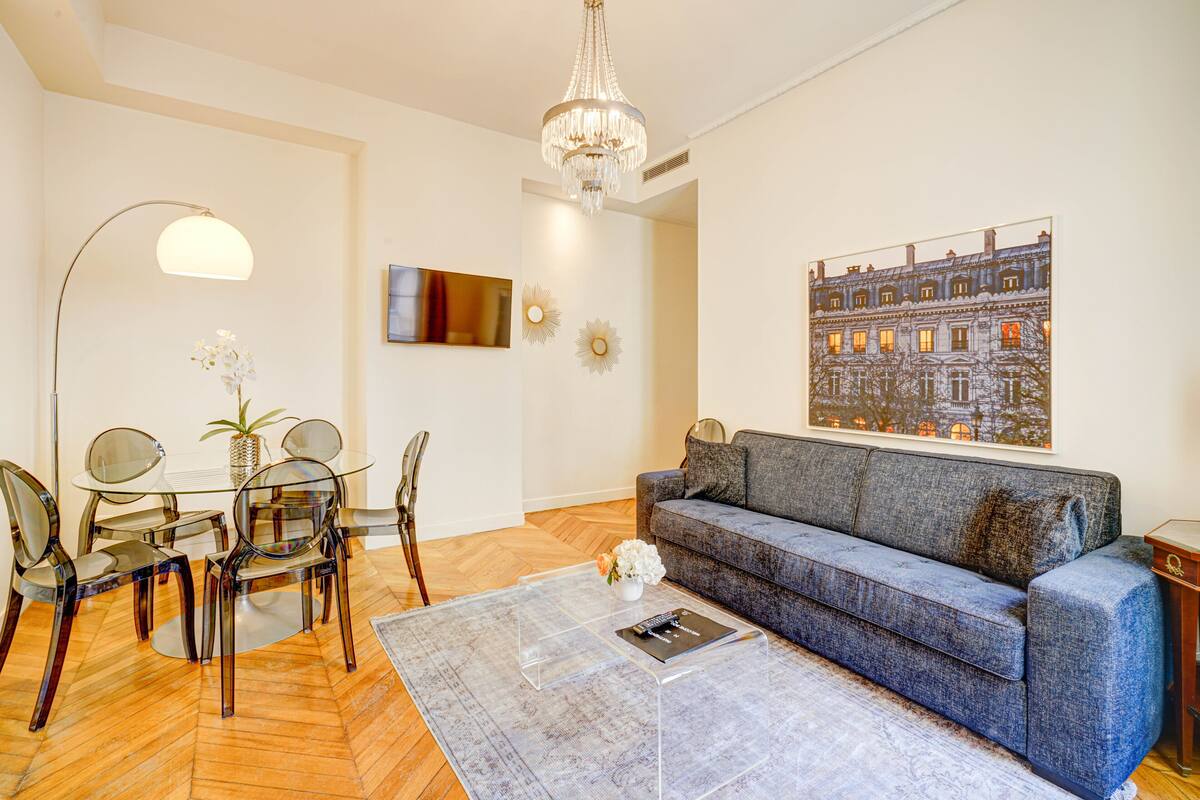 A modern living room with a glass coffee table, a blue sofa, and a chandelier.