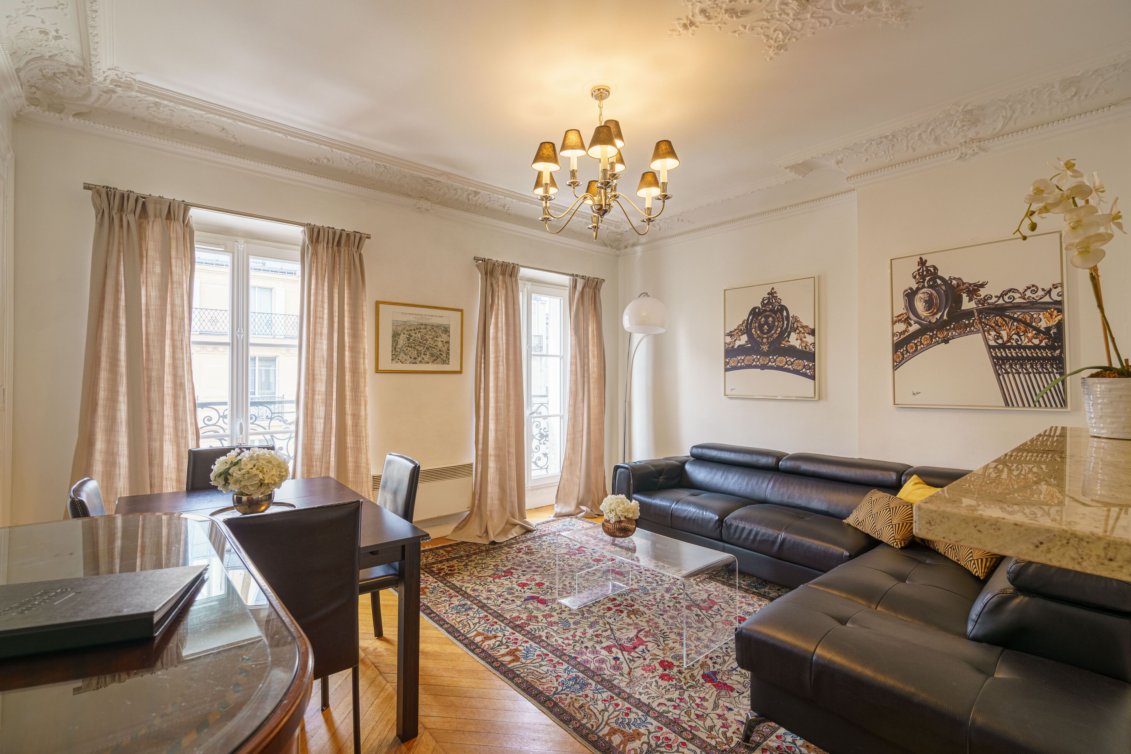 A living room with a sofa, a dining table with chairs, and a chandelier.