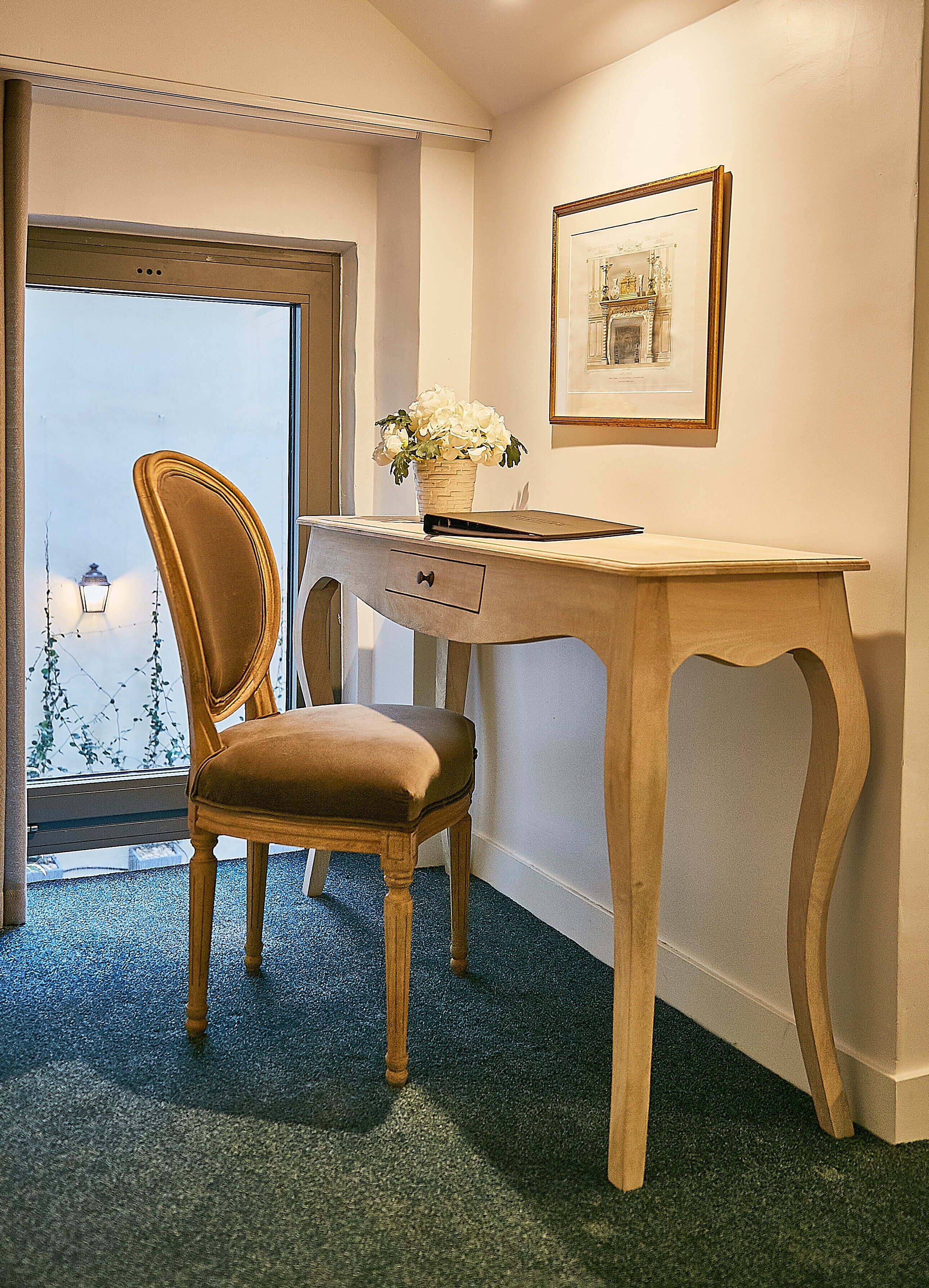 A room with a wooden desk, a chair, a vase with flowers, and a framed picture on the wall.
