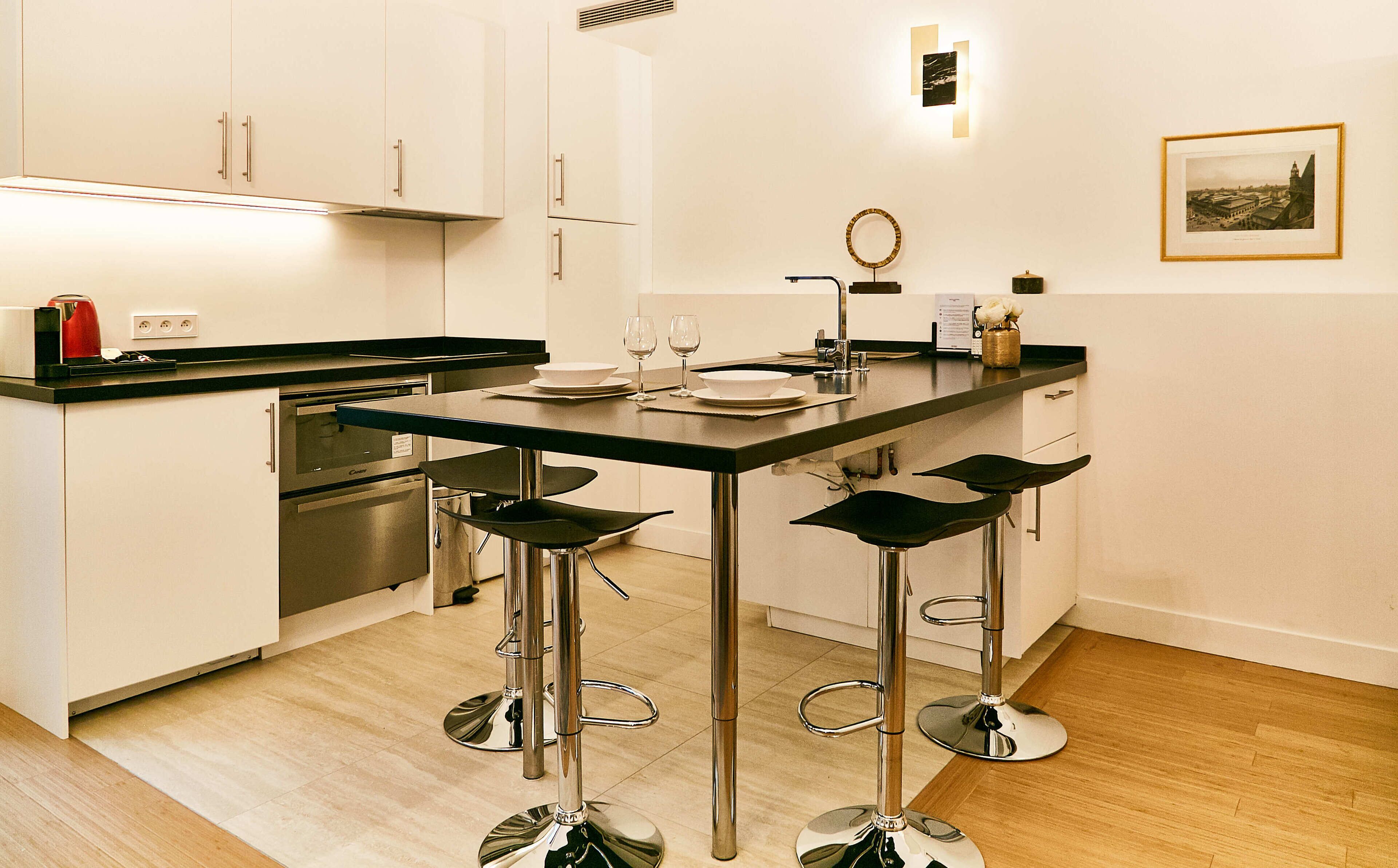 A modern kitchen with a central island, bar stools, and a dining table set for two.