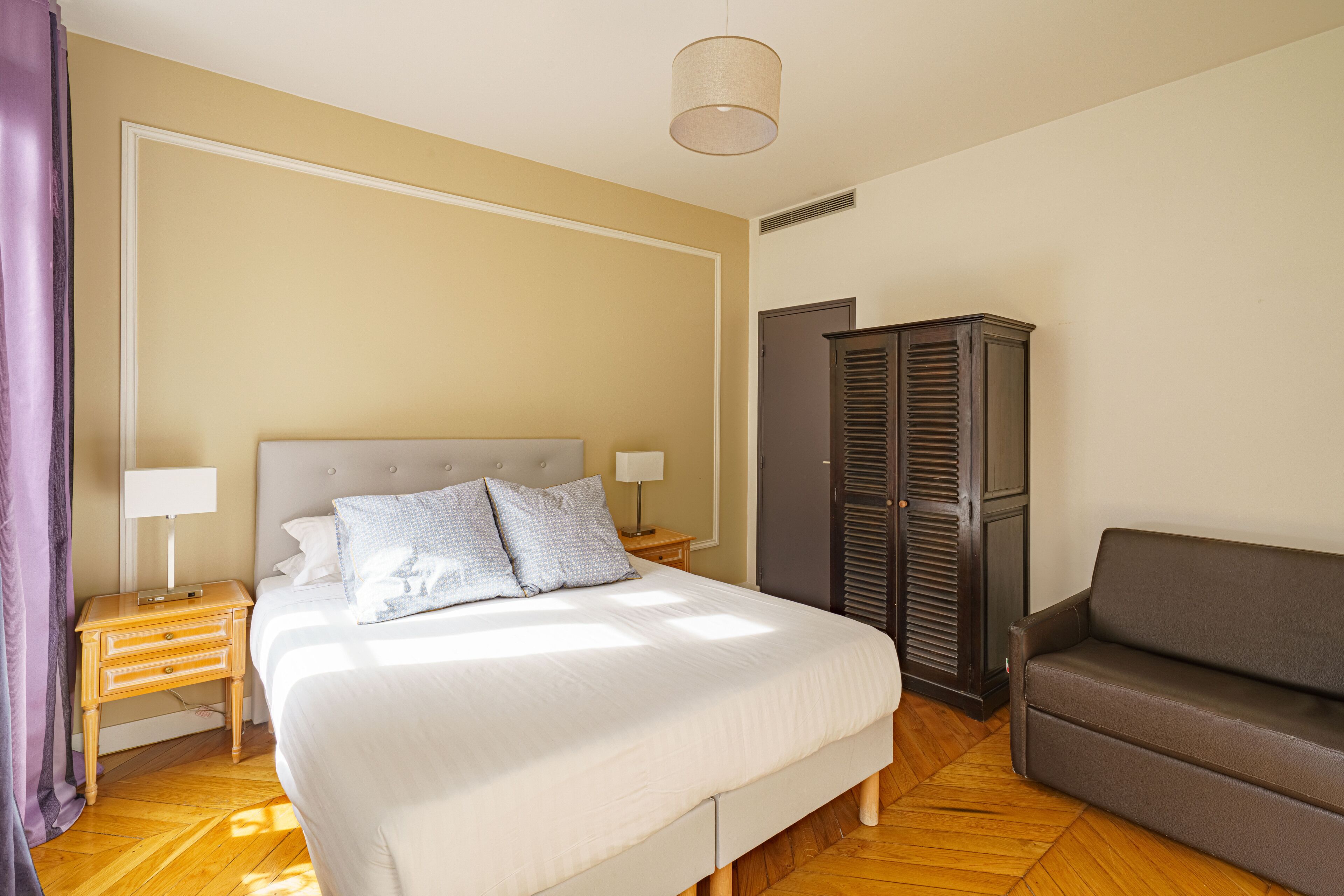 A bedroom with a bed, bedside tables, a wardrobe, and a sofa.