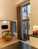 A modern living room with a sofa, a flat-screen TV, a window with curtains, and a view of the outside.