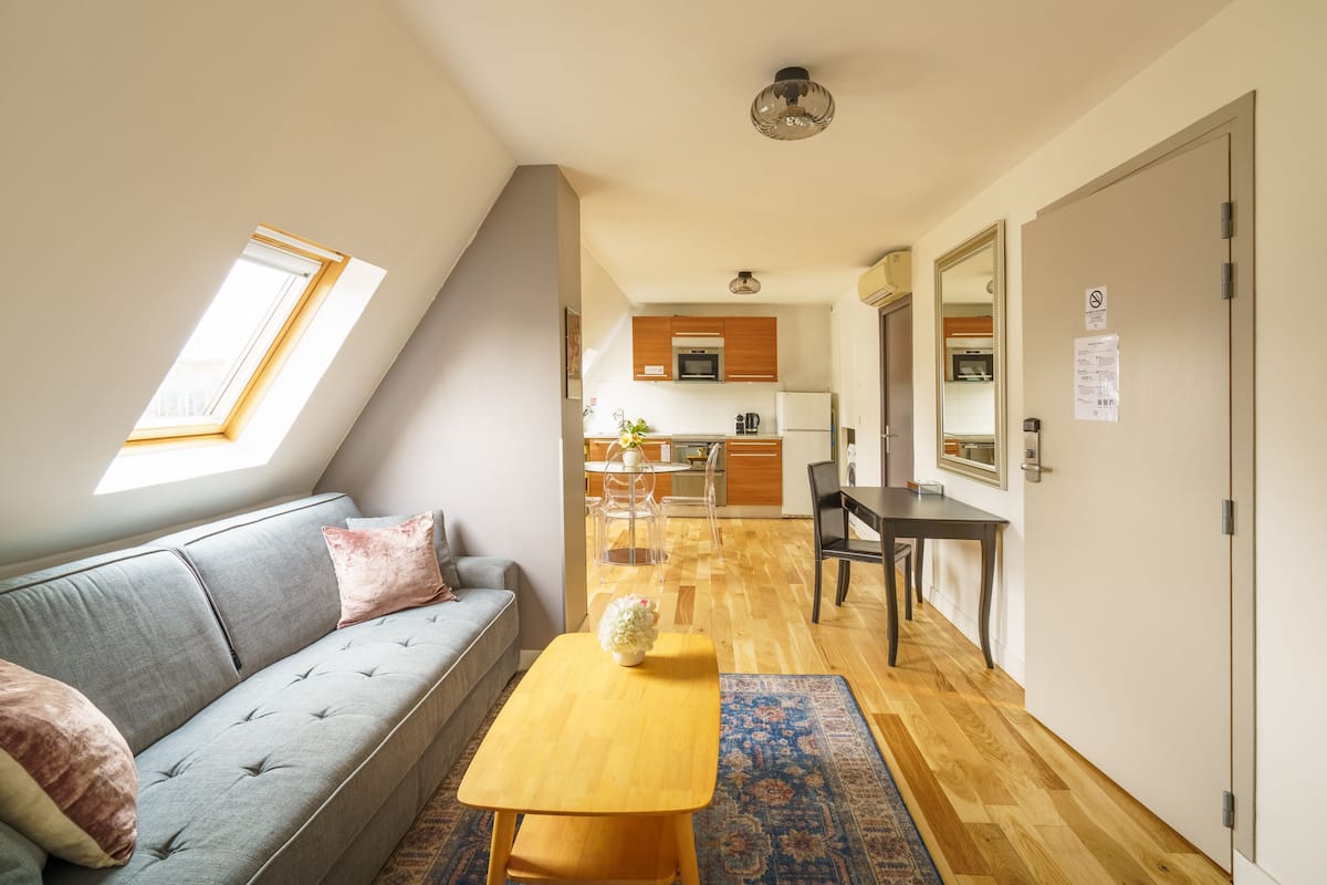 A compact living space with a sofa, a small wooden table, a kitchen area, and a dining table.