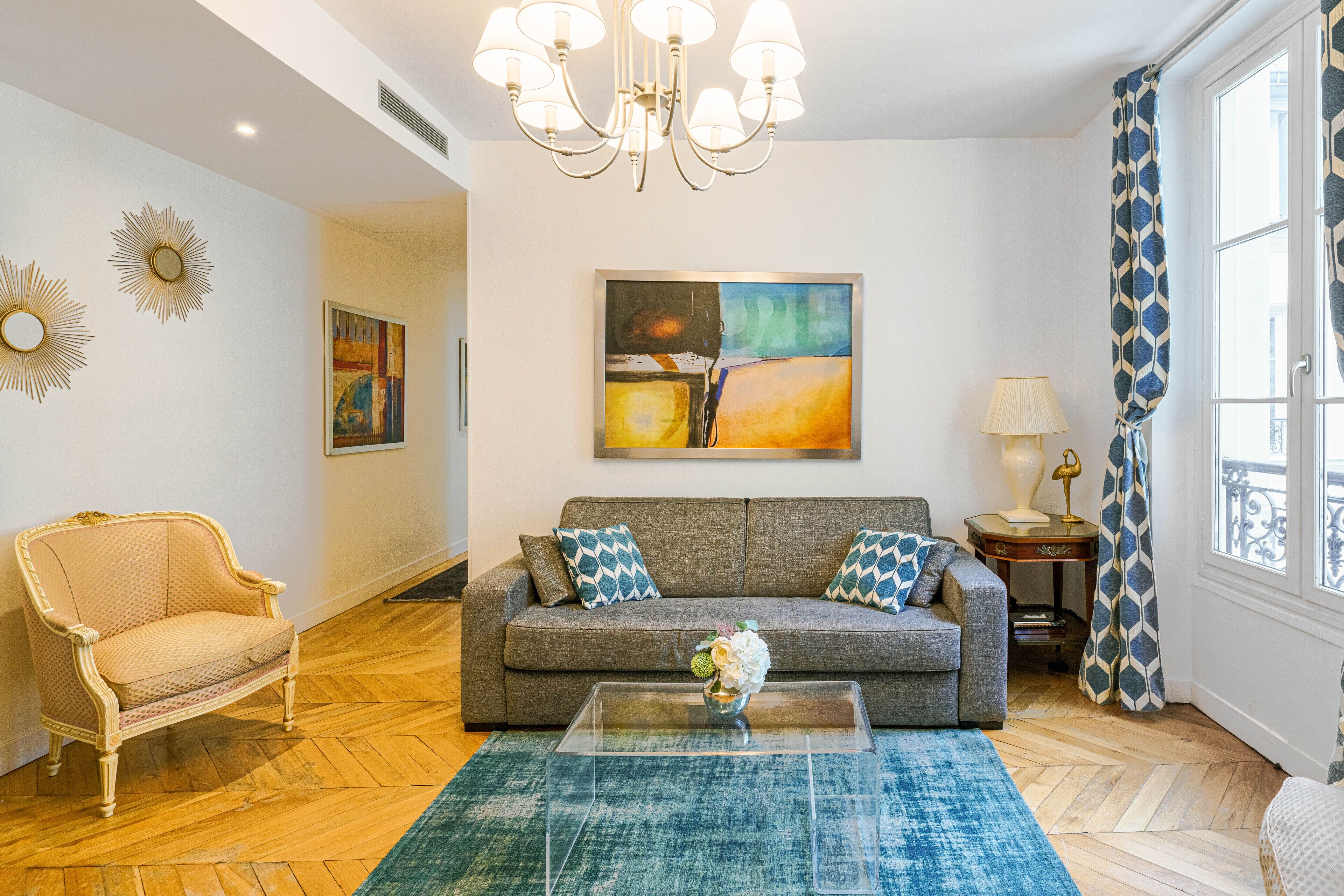 A living room with a sofa, a coffee table, a chandelier, and artwork on the wall.