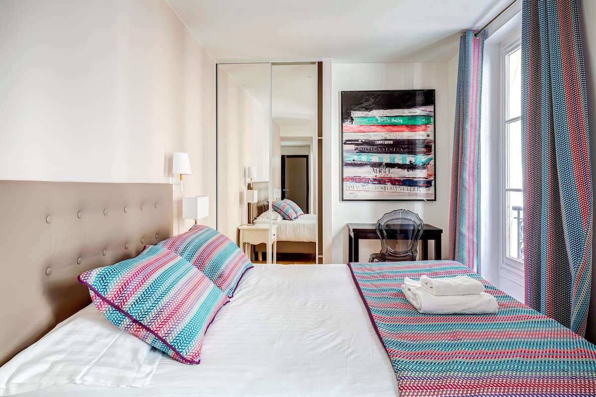 A hotel room with a large bed, a desk, a chair, and a mirror.