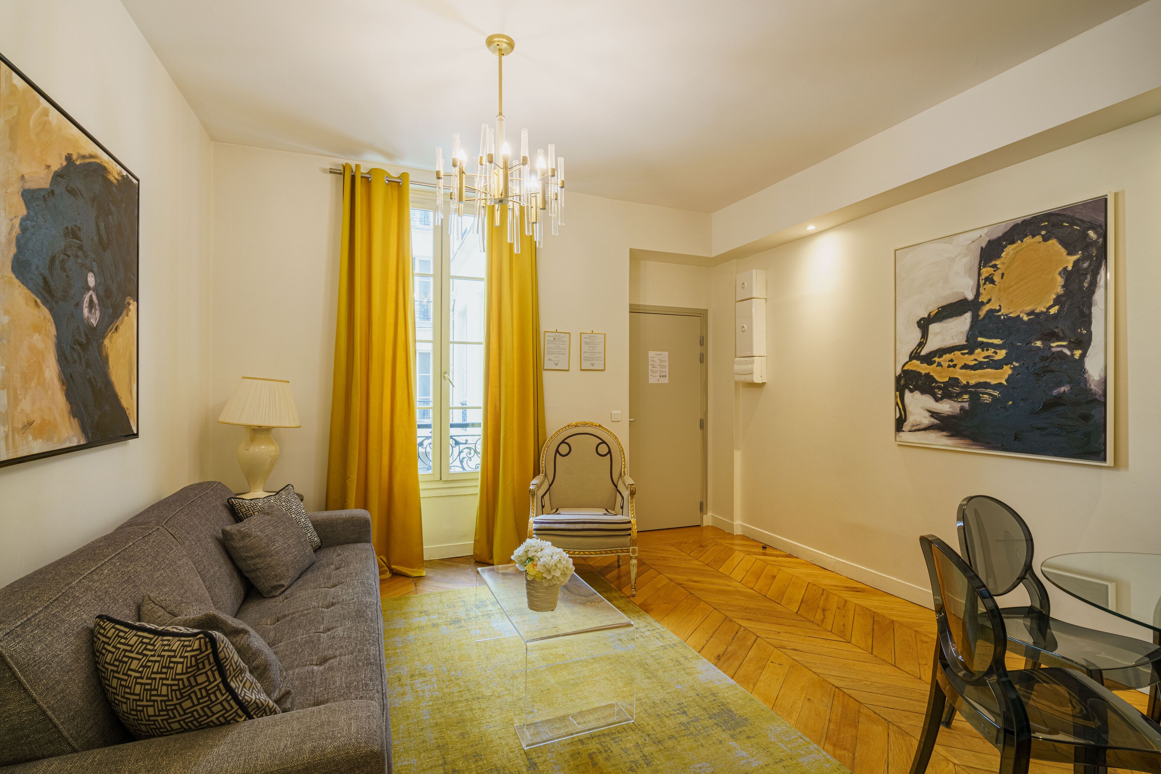 Un salon comprenant un canapé, une table basse en verre, un fauteuil, une table à manger et un lustre.