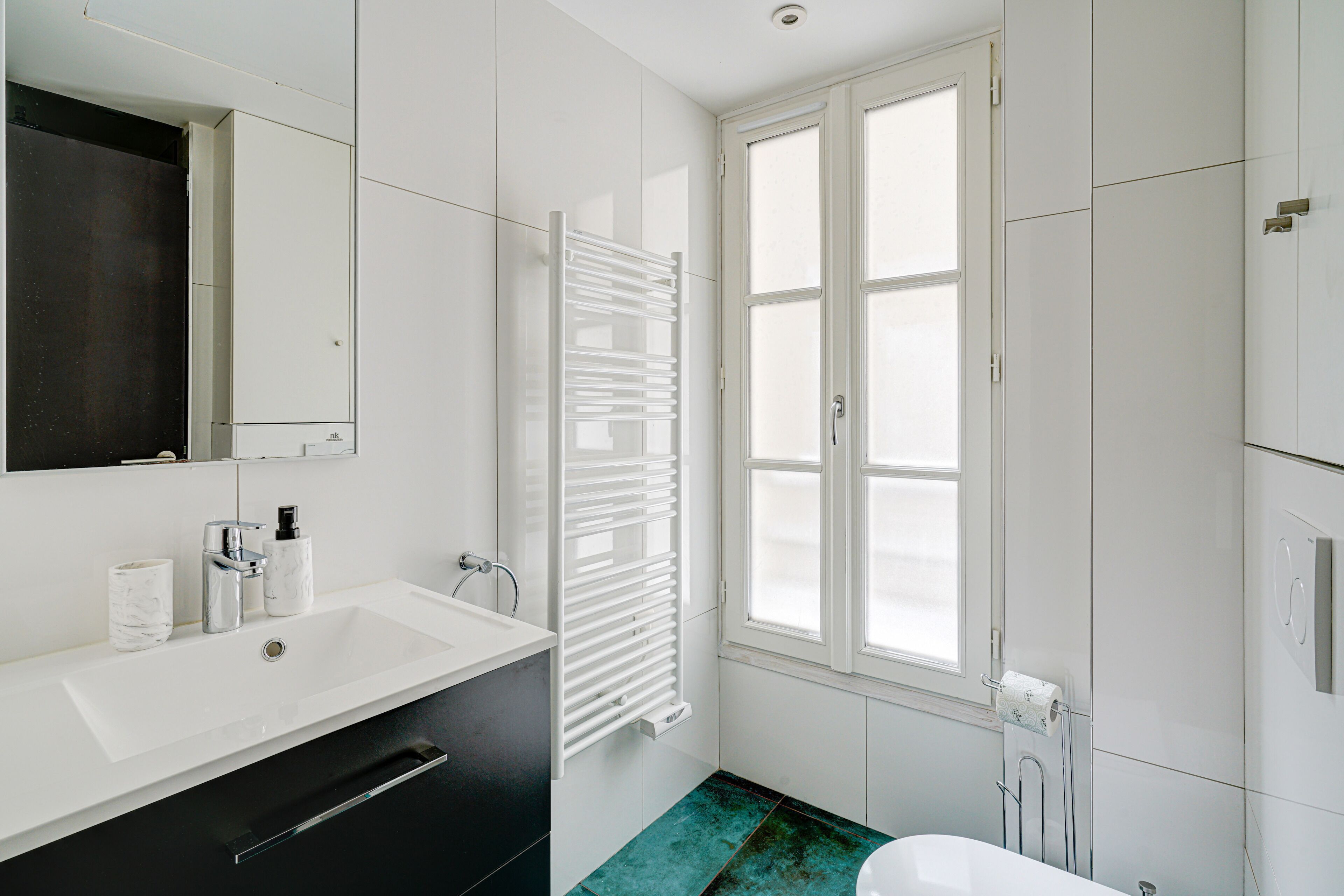 A modern bathroom with a white sink, mirror, and a window with blinds.