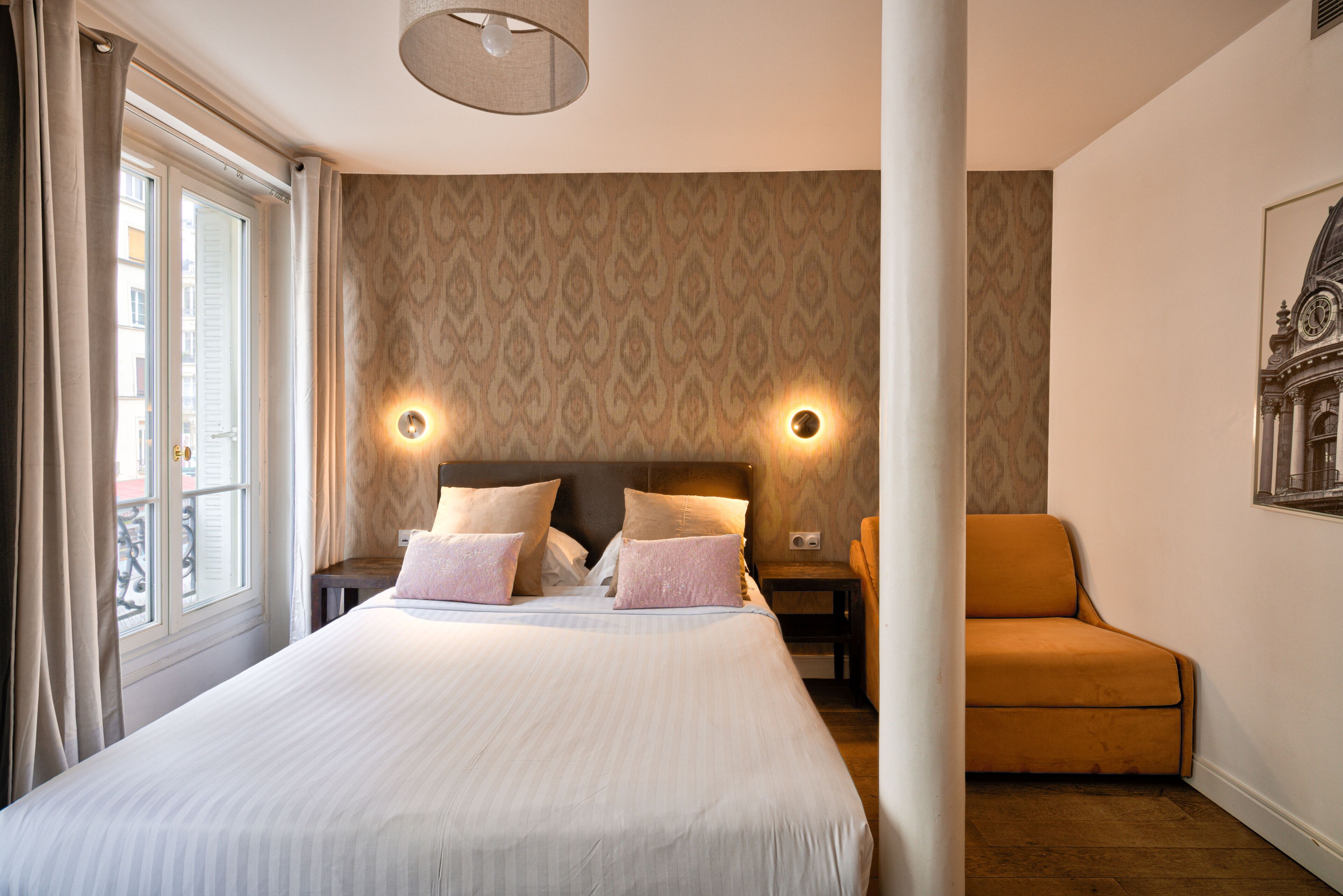 Une chambre d’hôtel avec un grand lit, deux tables de chevet, une petite table, un canapé et une fenêtre avec des rideaux.