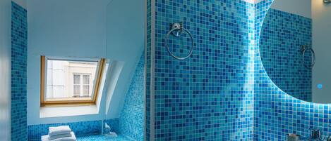Un baño moderno con azulejos de mosaico azules, un tragaluz, una bañera y un espejo grande.