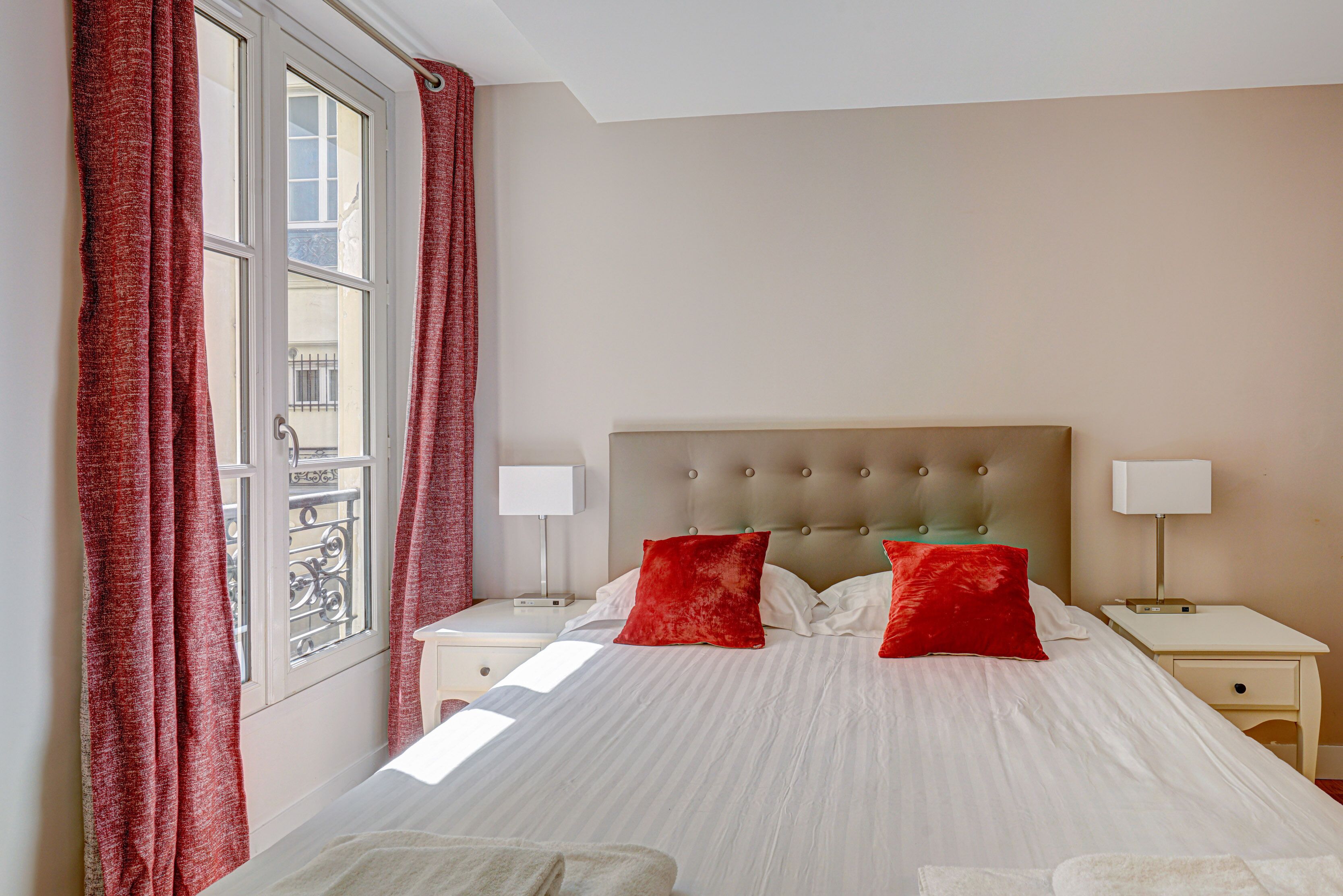 A neatly made bed with red pillows, a white headboard, and two bedside tables with lamps.