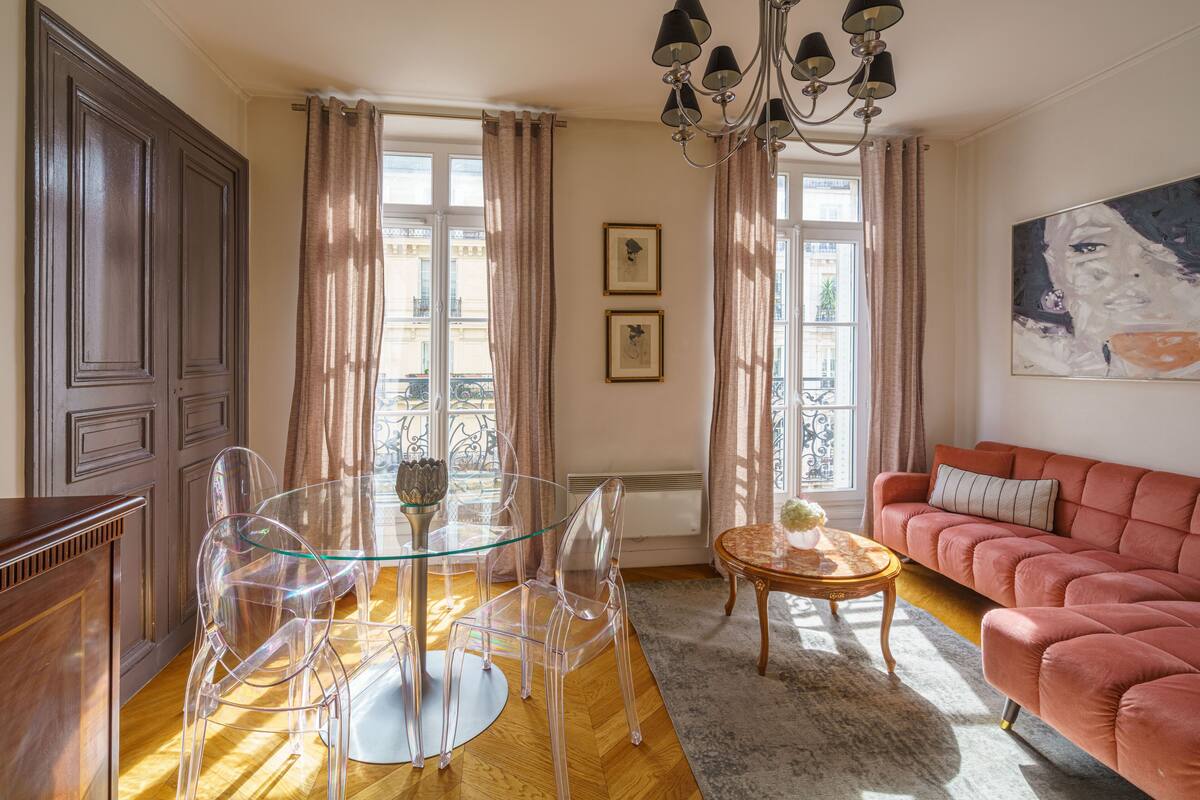 A living room with a glass table, clear chairs, a red sofa, and a chandelier.