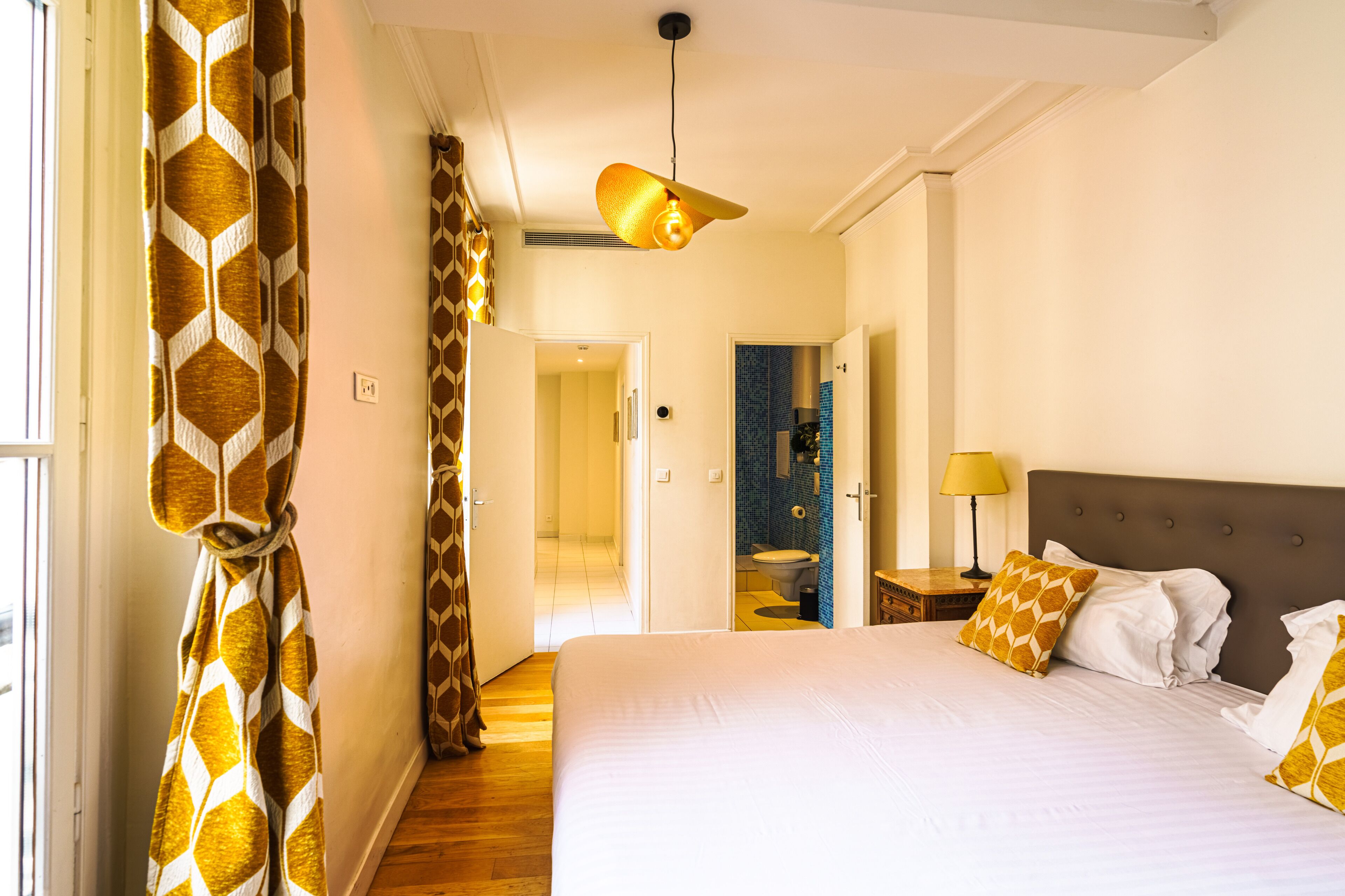 A hotel room with a large bed, a hanging light fixture, and a view of the bathroom.