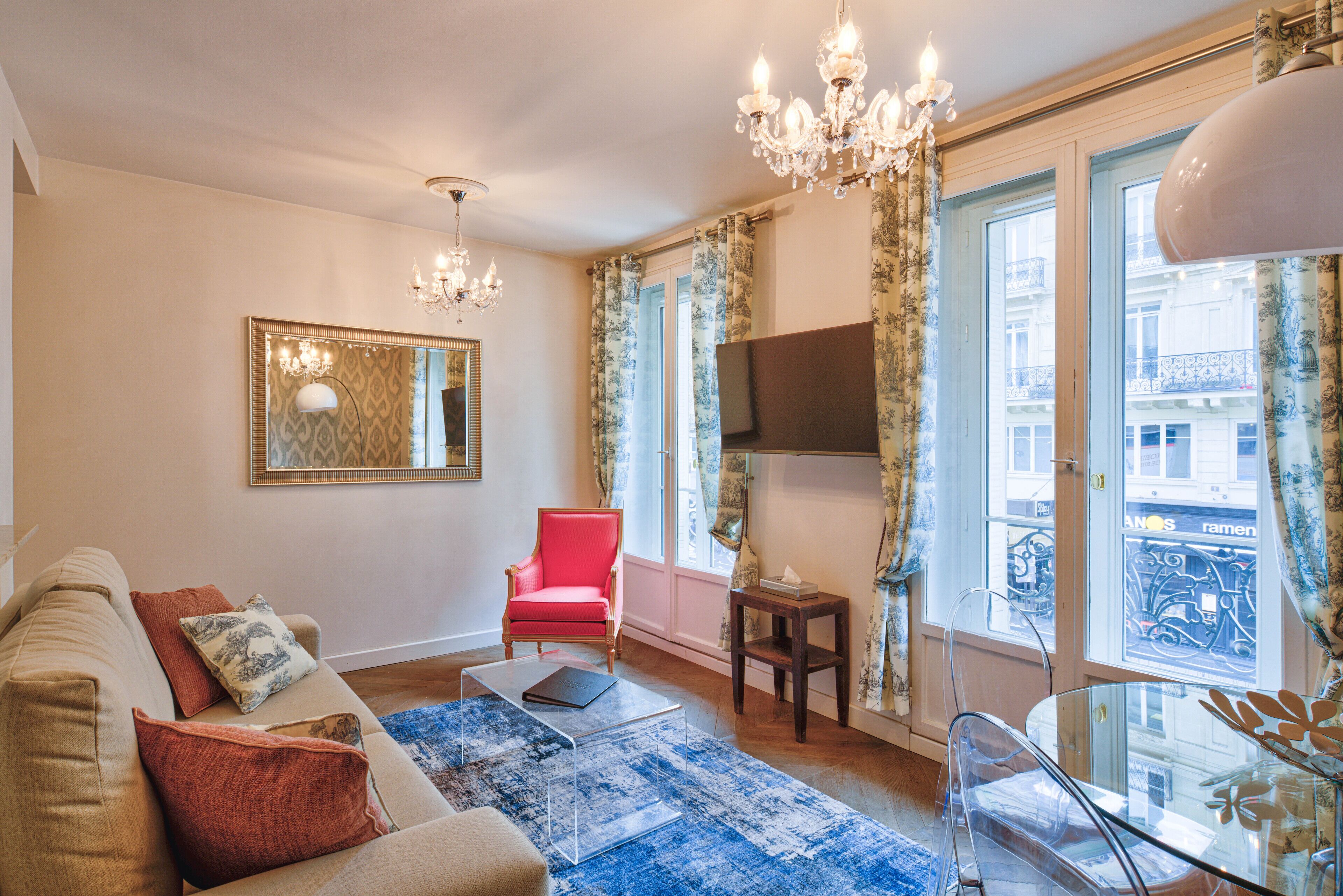 Un salon comprenant un canapé, un fauteuil rouge, une table basse en verre et un lustre.