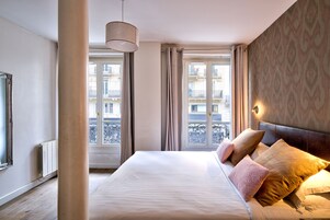 A hotel room with a large bed, a view of the city through the windows, and a modern design.