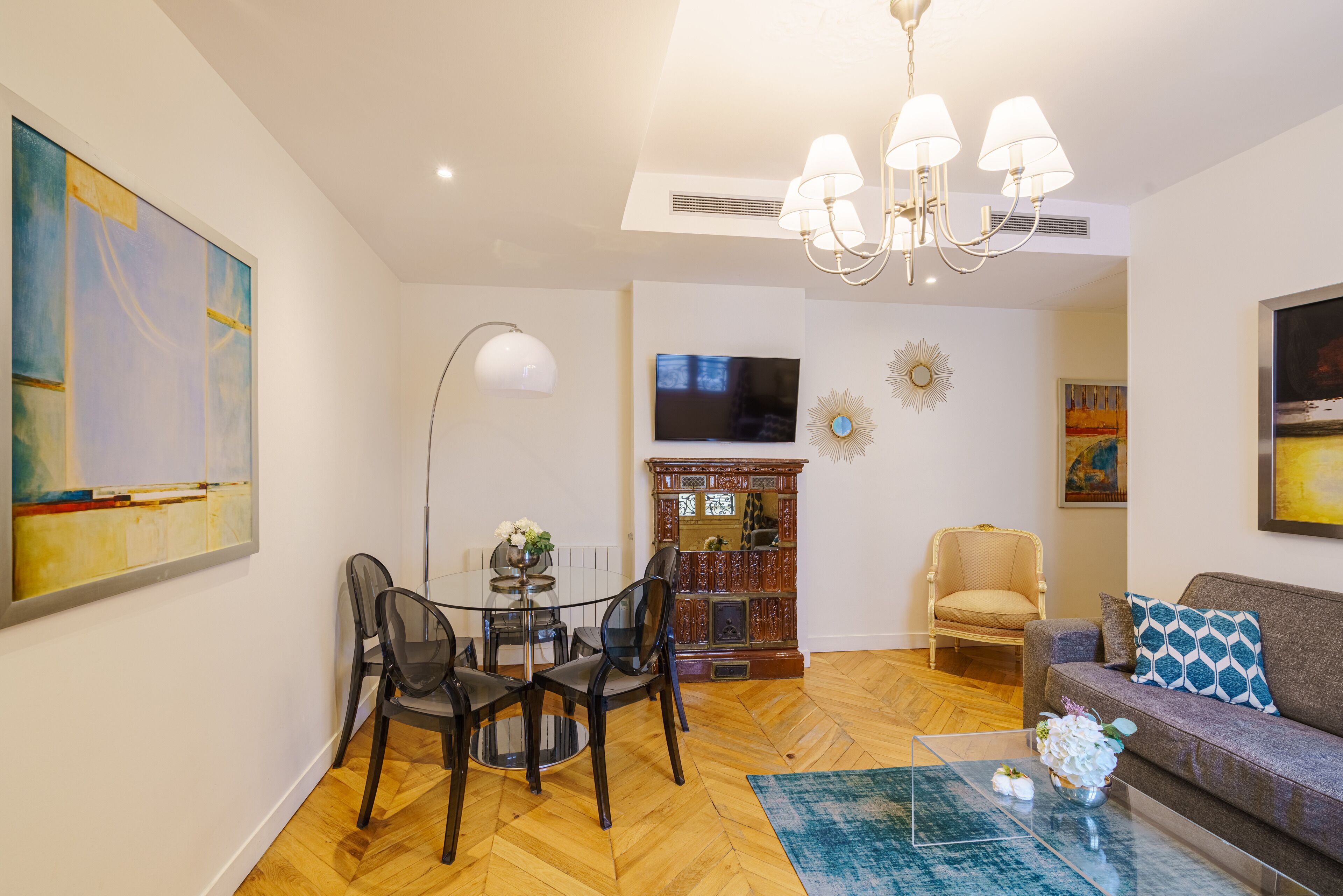 A living room with a sofa, a coffee table, a dining table with chairs, a TV, and artwork on the walls.