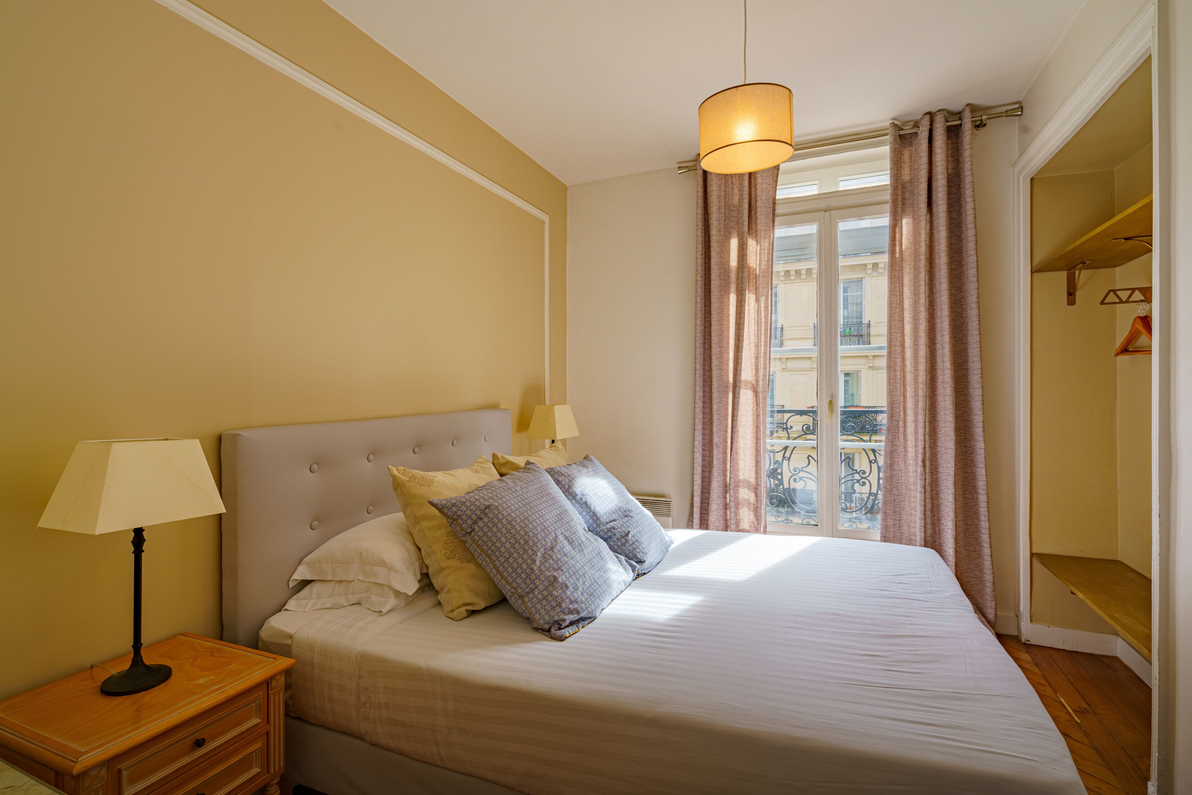 A neatly made bed with pillows, a bedside lamp, and a window with curtains.