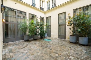 A courtyard with tiled flooring, potted plants, and large windows.