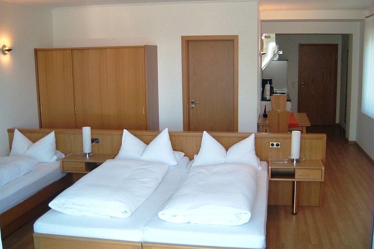 Une chambre d’hôtel avec deux lits simples, des armoires en bois, un petit bureau et une salle de bain visible à travers une porte ouverte.