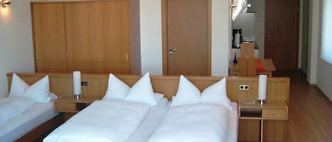 Habitación de hotel con dos camas individuales, armarios de madera, un escritorio pequeño y un baño visible a través de una puerta abierta.
