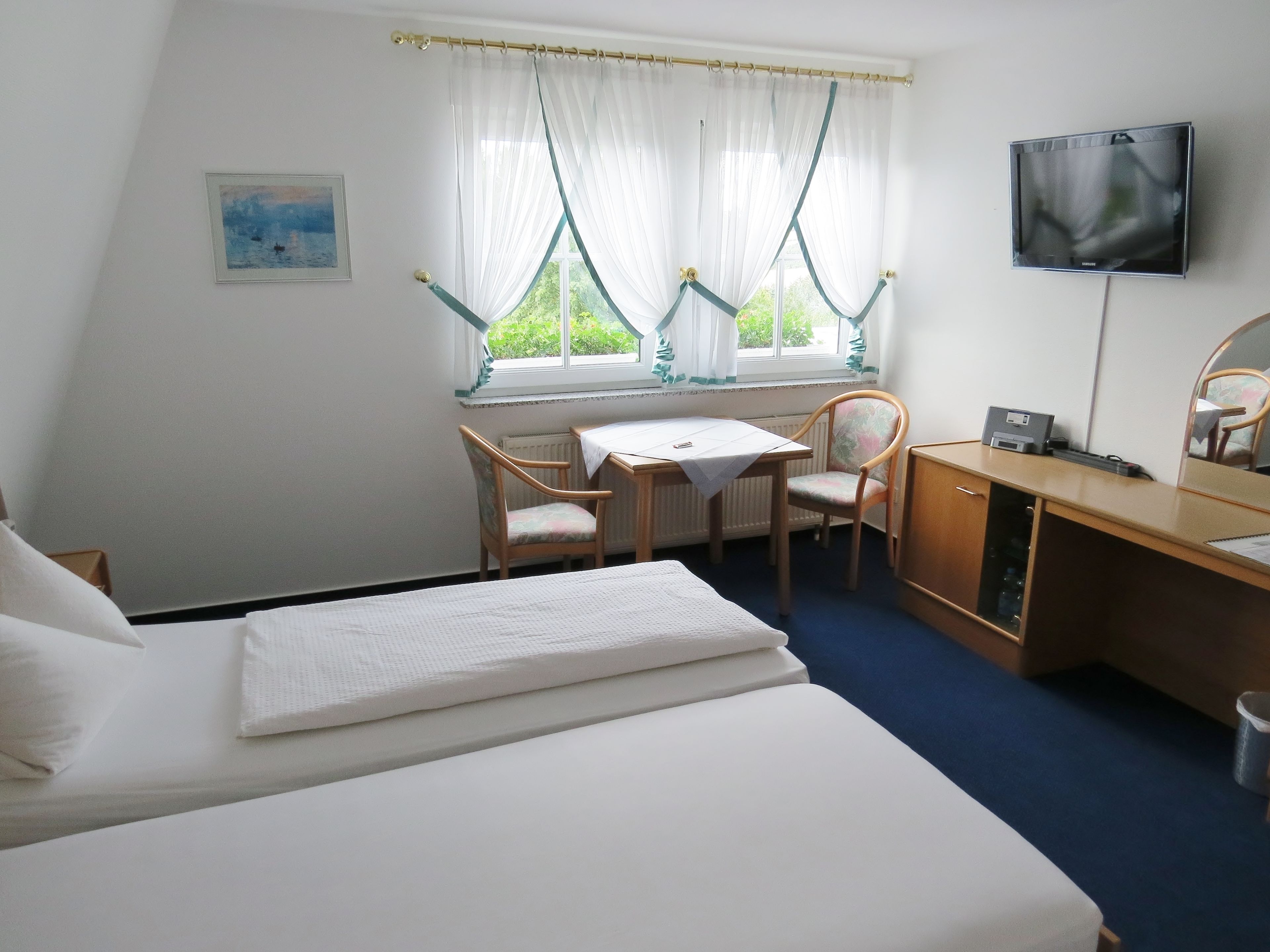 A hotel room with a bed, a desk, two chairs, a TV, and a window with curtains.