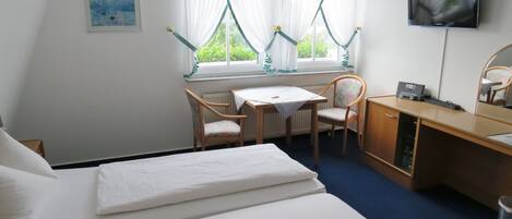 A hotel room with a bed, a desk, two chairs, a TV, and a window with curtains.