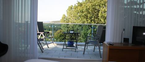 A hotel room with a balcony, a bed, a TV, and a desk with a chair.