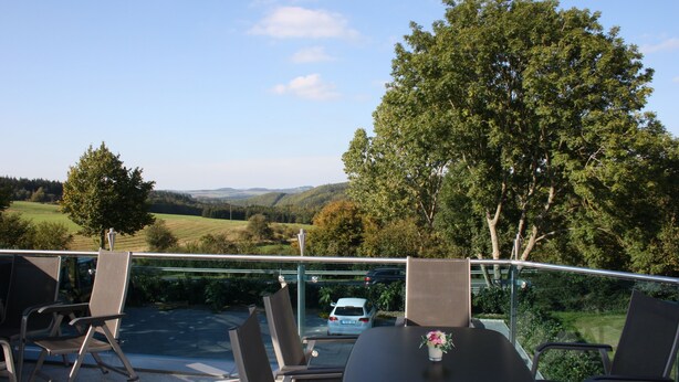 A terrace with a table and chairs, overlooking a road and greenery. - Hotel Retterath am Nürburgring (Wiesemscheid)