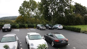 A parking lot with several cars, including a white Porsche and a black Audi, surrounded by greenery and trees.
