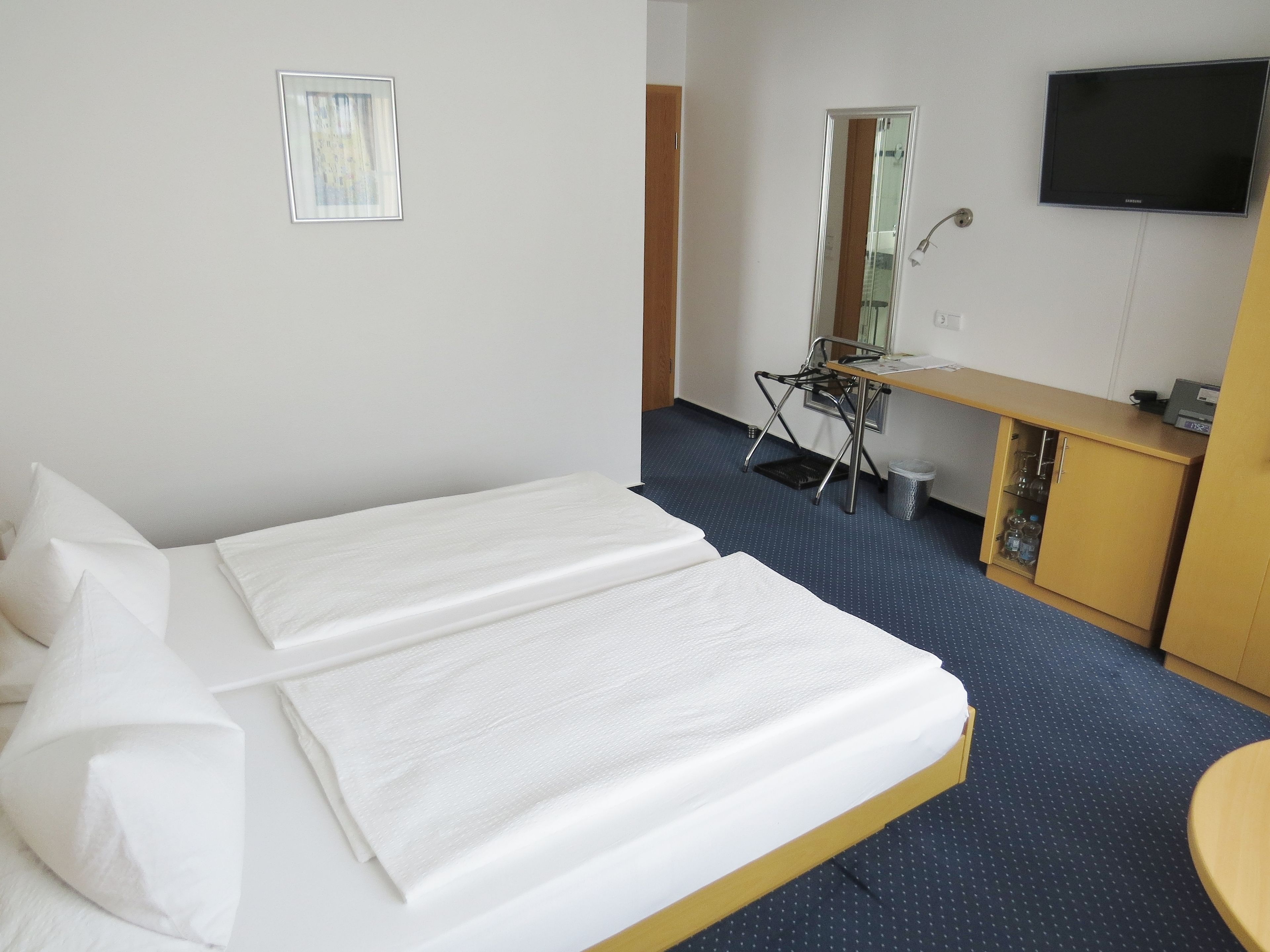 Una habitación de hotel con cama, escritorio, silla, televisor y un mueble pequeño.