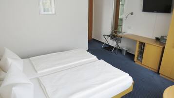 Una habitación de hotel con cama, escritorio, silla, televisor y un mueble pequeño.