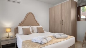Una cama bien hecha con cabecera, una lámpara de noche y un juego de toallas sobre la cama.