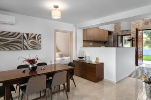 A modern kitchen with wooden cabinets, a stainless steel refrigerator, and a dining area with a wooden table and chairs. - Sperveri Enalio Villas (Rhodes)