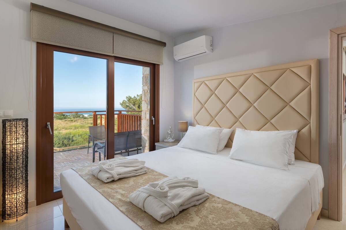 Habitación de hotel con una cama grande, vistas al mar y un balcón con mesa y sillas.