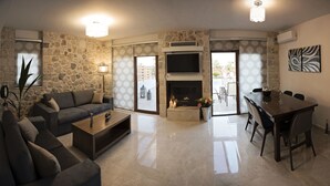 Una sala de estar con pared de piedra, chimenea, televisor y comedor.