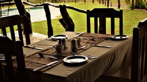 Mesa de comedor preparada para cuatro personas con vista a una piscina y al paisaje.