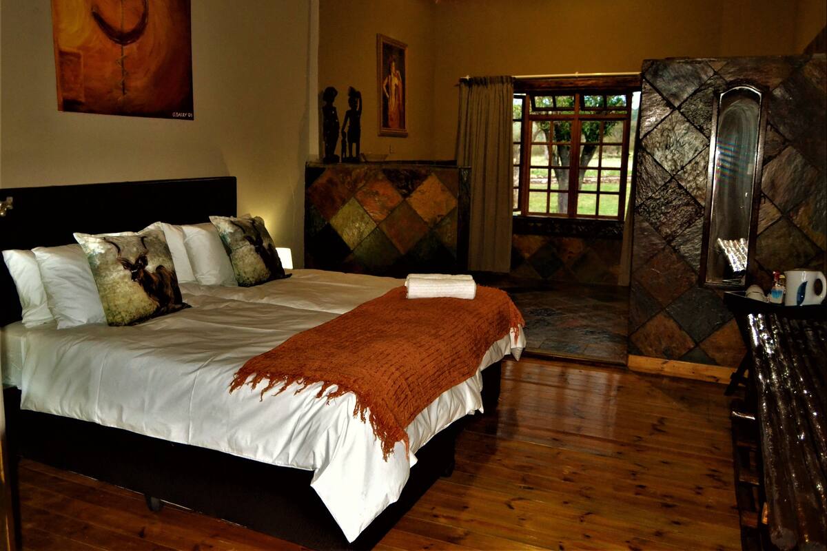 A bedroom with a bed, a painting on the wall, a window with curtains, and a stone wall.