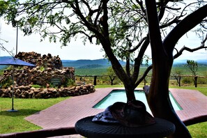 Zona de piscina con una estructura de piedra, vistas del paisaje y un árbol que da sombra.