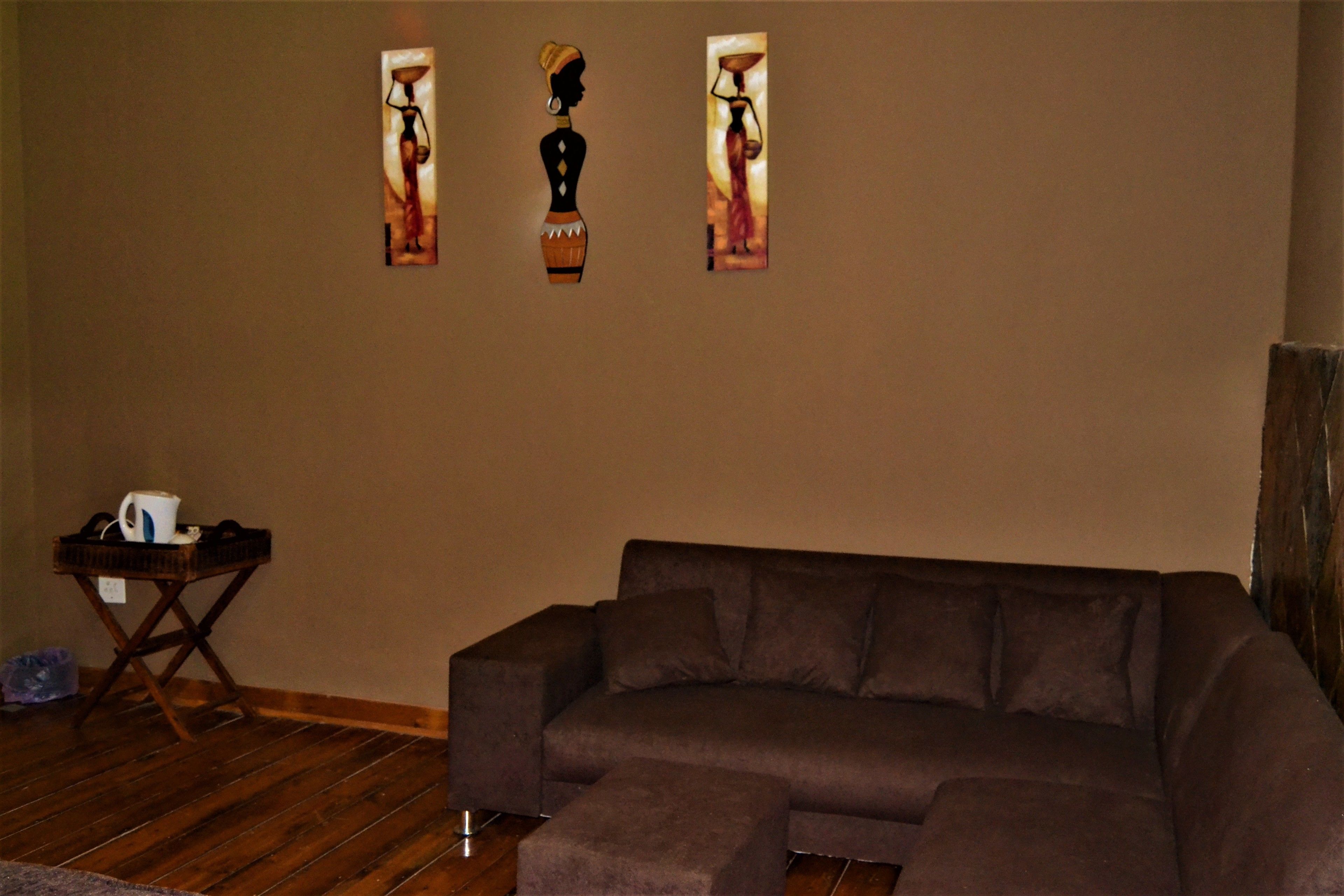 A living room with a sectional sofa, a small wooden side table, and three wall-mounted paintings.
