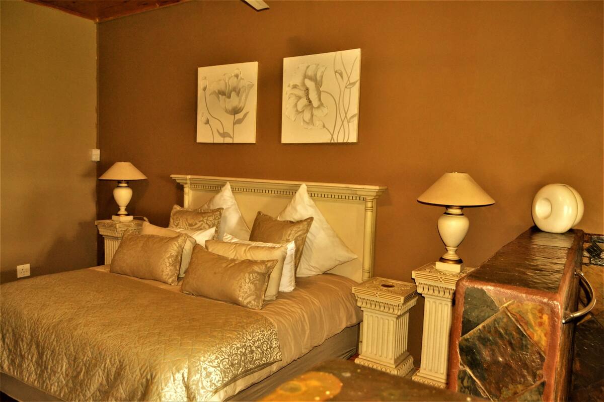 A bedroom with a large bed, two bedside tables with lamps, and two wall-mounted floral paintings.