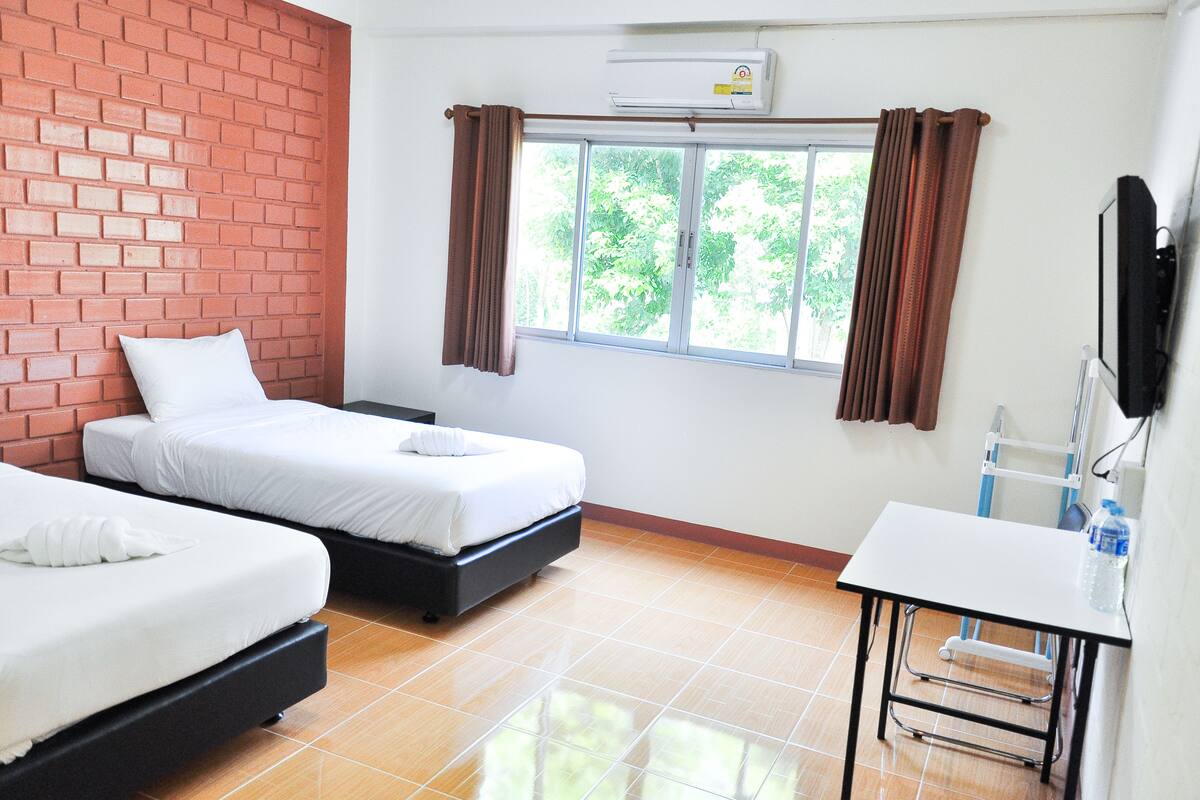 A hotel room with two beds, a TV, a desk, and a window with curtains.