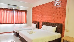 A hotel room with two beds, a brick-patterned wall, a window with red curtains, and a small wooden table. - Budsarakam Place Hotel (Chanthaburi)