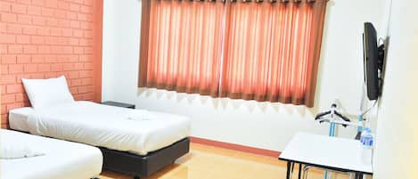 A hotel room with two beds, a desk, a TV, and a window with curtains.
