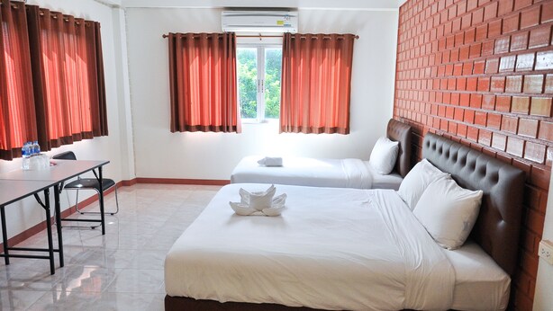 A hotel room with two beds, a desk, and a brick wall. - Budsarakam Place Hotel (Chanthaburi)