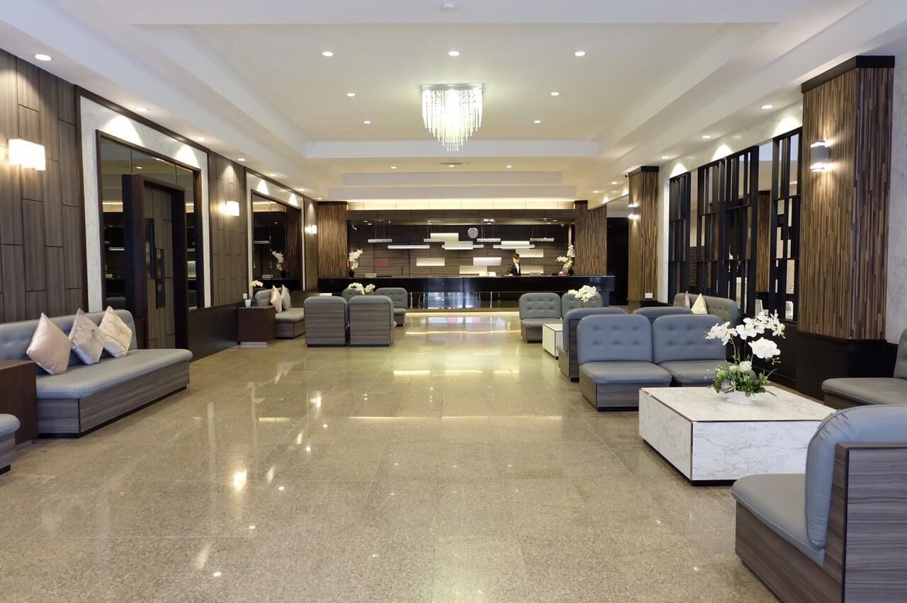 A modern lobby with a central reception desk, seating area with sofas and armchairs, and a chandelier.