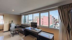 A modern hotel room with a large window, a sofa, a desk, and a refrigerator. - The Grand Day Night (Pattaya)