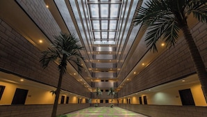 A spacious indoor area with a high ceiling, a central atrium, and a symmetrical layout with palm trees and green carpeted areas. - The Grand Day Night (Pattaya)