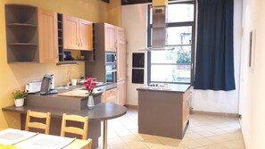 A compact kitchen with wooden cabinets, a built-in oven, a microwave, and a gas stove. There is a small dining area with a table and chairs, and a window with a view of the outside. - Chez Esmara et Philippe (Brussels)
