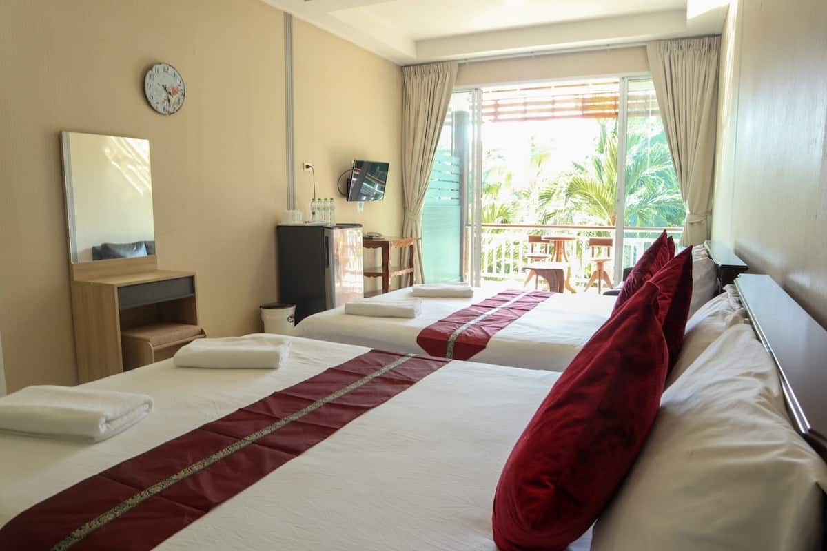 Une chambre d’hôtel avec deux lits, une télévision, un minibar, un bureau et un balcon offrant une vue sur les palmiers.
